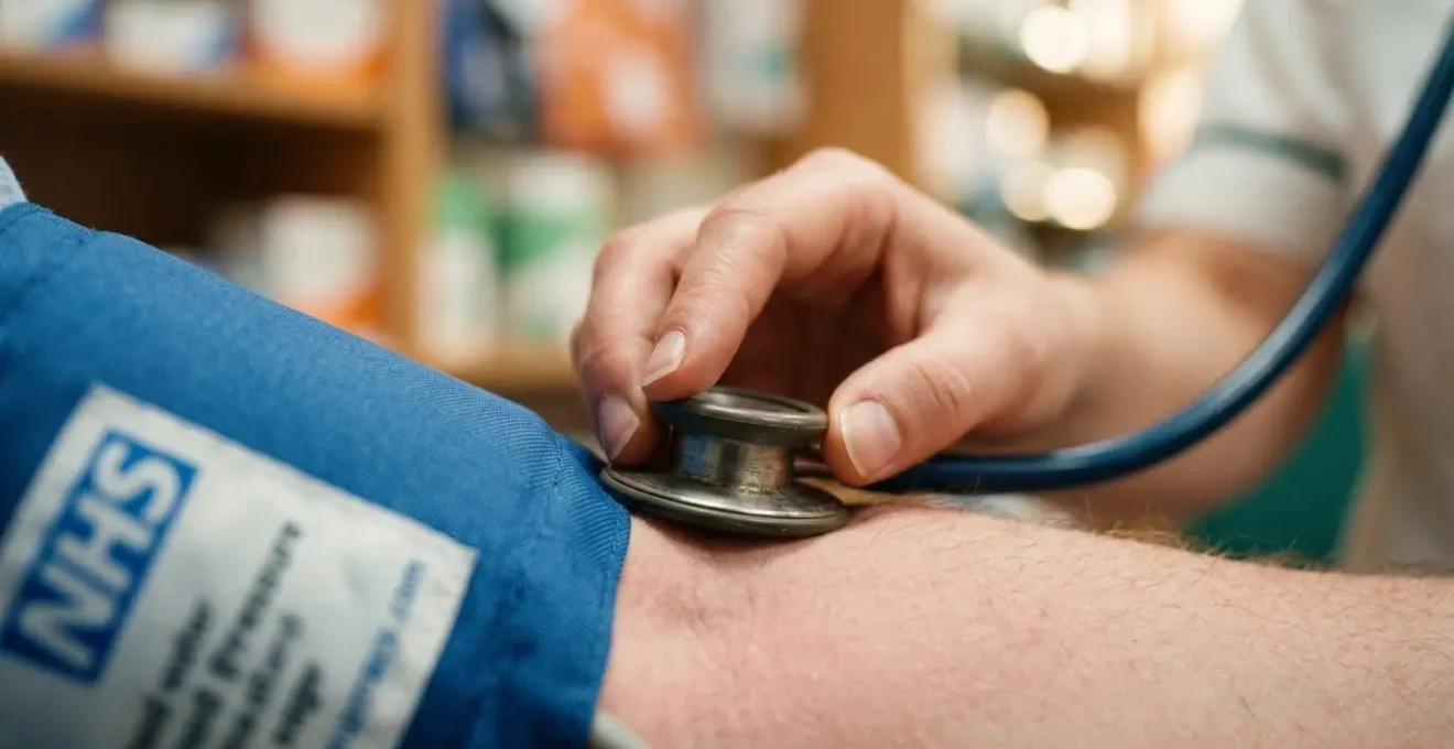 British pharmacist conducting blood pressure screening in private consultation room at community pharmacy