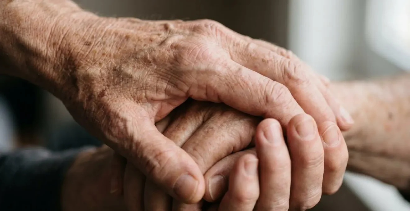 Macro detail of weathered hands clasped together showing texture of age and care burden, photographed with extreme shallow depth of field